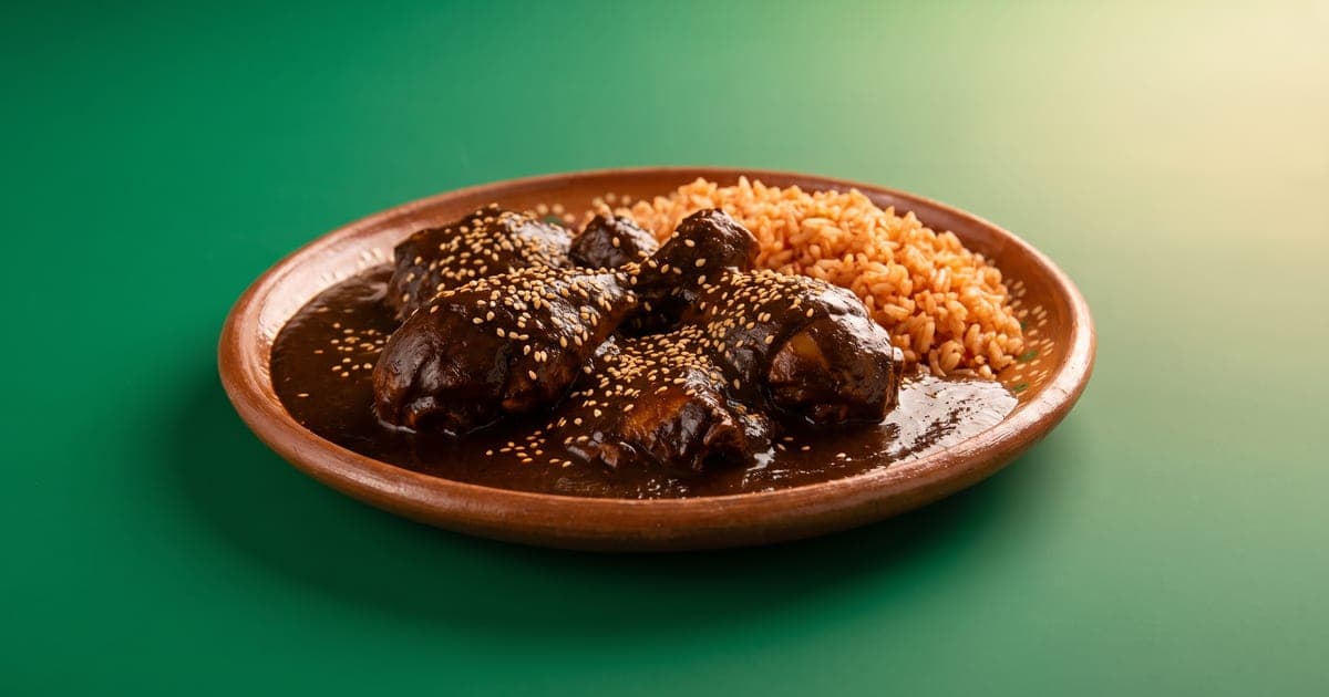 Plato de mole poblano con pollo, ajonjolí y arroz rojo, sobre fondo verde